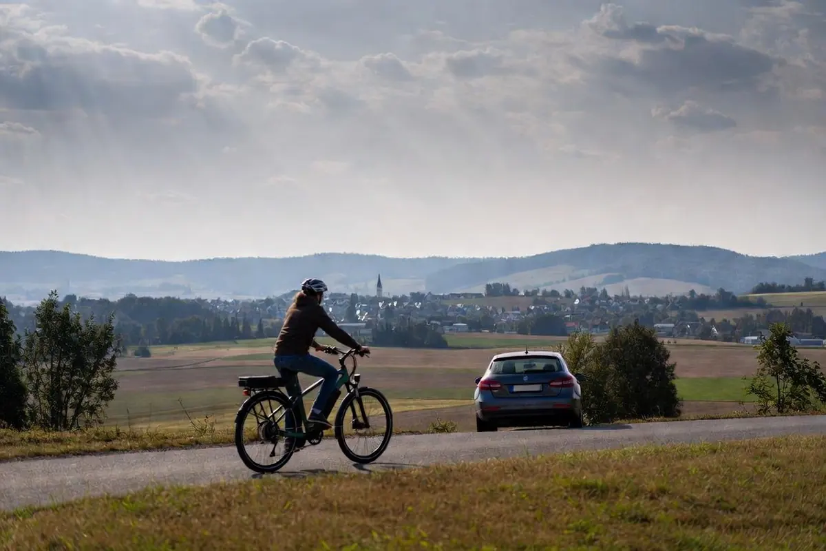 Frau auf dem e-Bike und ein Auto auf einer Landstraße in Niederösterreich – KFZ- und e-Bike-Versicherung